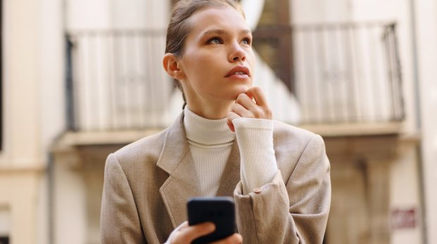 A Young Woman Deep in Thought as She Engages with Her Smartphone in a Bustling Urban Setting