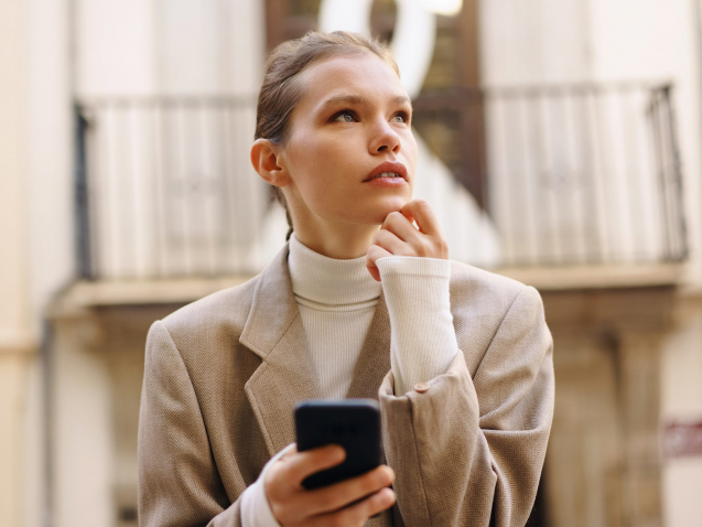 A Young Woman Deep in Thought as She Engages with Her Smartphone in a Bustling Urban Setting